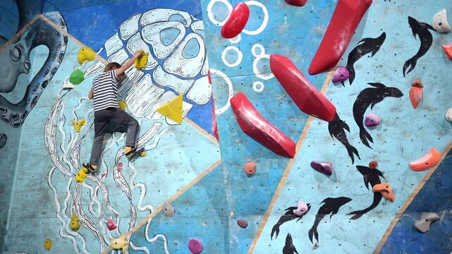 6-year-old boy practicing bouldering on a colorful indoor climbing wall. Focused and determined, he navigates different holds, showcasing strength and balance.