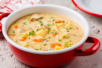 Chicken stew in creamy sauce with potatoes and carrots in red saucepan. Comfort food concept.