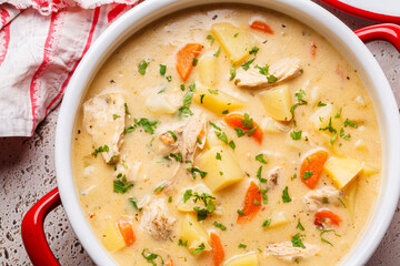 Chicken stew in creamy sauce with potatoes and carrots in red saucepan. Comfort food concept.