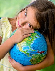 A young child lovingly hugs a model of planet Earth, symbolizing the importance of protecting the...