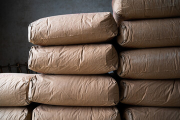 A stack of bags of cement. The bags are brown and stacked on top of each other. The bags are piled...