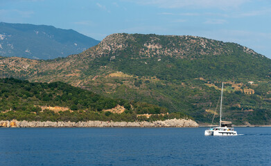Fototapeta premium Sailboat sailing on a vast blue sea on a sunny day with cloudy sky near shore of Greek island