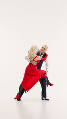 Full-length image of senior couple, man and woman dressed in elegant red dress and black classic...