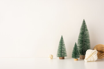 Decorative side view setup with mini snow-covered Christmas trees and paper ornaments in a Scandinavian minimalist style, placed against a neutral backdrop