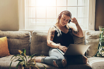 Laptop, headphones and woman on sofa in home listening to music for freelance playlist curator career. Relax, audio tech and female person with computer for streaming podcast in living room at house.