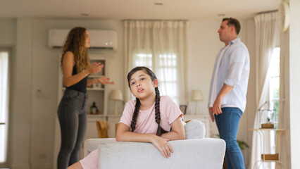Obraz premium Annoyed and unhappy young girl sitting on sofa trapped in middle of tension by her parent argument in living room. Unhealthy domestic lifestyle and traumatic childhood develop to depression Synchronos