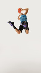 Male basketball player in tank top and shorts makes powerful jump, preparing for slam dunk against grey studio background. Low angle. Concept of sport event, competition, healthy lifestyle, game. © Lustre Art Group 