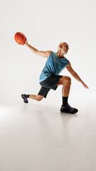 Naklejka premium Low angle photo of middle aged man in sleeveless jersey and shorts, training dribbling technique against grey studio background. Concept of sport event, competition, active and healthy lifestyle, game