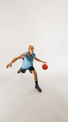 Male basketball player dressed in sports gear dribbles ball, focusing on his next move against grey studio background. Concept of sport event, competition, active and healthy lifestyle, game.