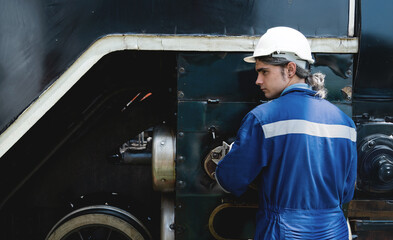 A man in a blue and white uniform is working on a train engine. He is wearing a hard hat and gloves