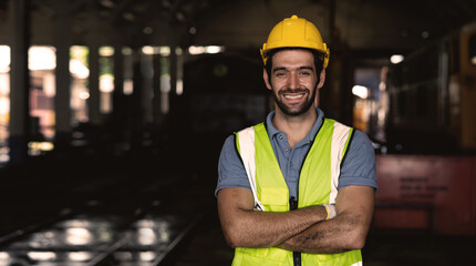 A man in a yellow safety vest is smiling and posing for a picture. He is wearing a hard hat and is standing in a dark room