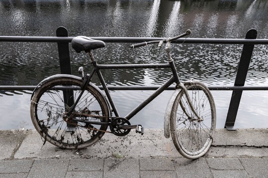 A rusted and weathered bicycle rests by a canal, its frame showing signs of age and neglect, adding to the urban and nostalgic atmosphere of the scene.