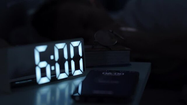 Man waking up, turning off alarm clock on digital clock and smartphone. Sleepy man waking up at 6 o'clock morning