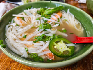 A bowl of pho with noodles, shrimp, and vegetables. The soup is green and has a red spoon. Vietnamese restaurant