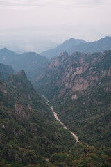 Fototapeta premium Aerial view of a valley with a dry river and a Chinese city in the background that almost cannot be seen due to the fog and air pollution, autumn in the Yellow Mountain, Huangshan, China