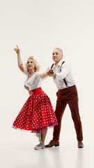 Joyful elderly couple dancing in matching retro outfits with energy and passion to retro dance...