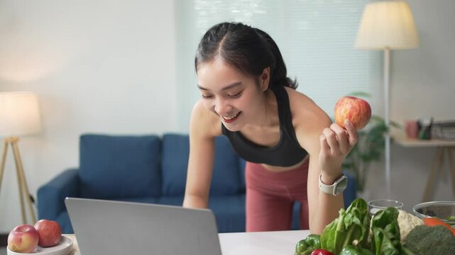 Smiling nutritionist holds an apple while conducting an online meeting with a client on a laptop at home