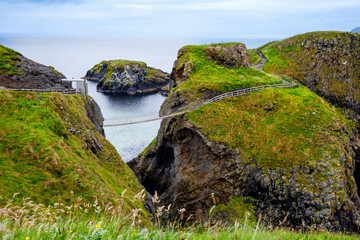 View from Carrick-a-Rede Rope Bridge, famous rope bridge near Ballintoy in County Antrim, Northern Ireland on Irish coastline. Tourist attraction, bridge to small island on cloudy day.