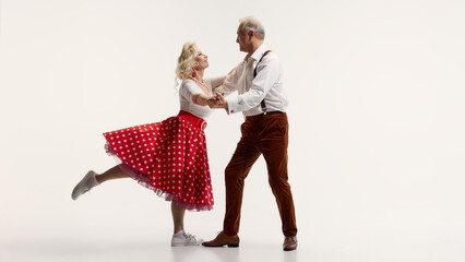 Cheerful elderly couple dancing together, woman in red polka dot skirt and man in suspenders isolated on white background. Concept of retro dance, hobby, aging, active lifestyle