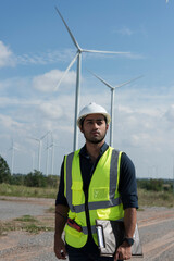 Male engineers with drawing against turbines on wind turbine farm.