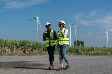 Couple engineers with drawing against turbines on wind turbine farm.
