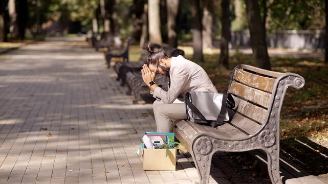 Stressed businessman sitting on bench in park after job loss