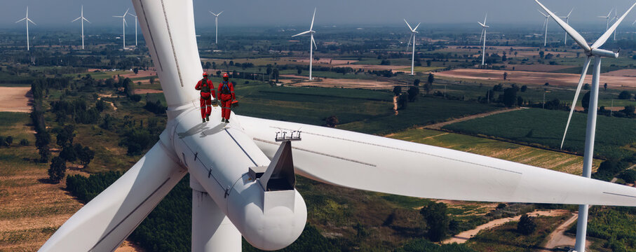 Wind mill engineer wearing PPE standing on wind turbine.. Engineering or Worker standing a top of windmill and looking beautiful Landscape.