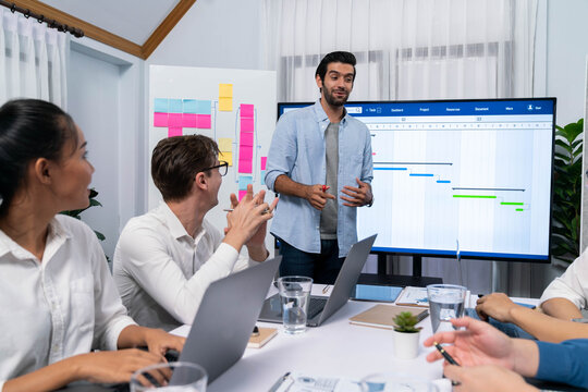 Project manager communicate and collaborate with team using project management software display on monitor, tracking progress of project task and making schedule plan at meeting table. Prudent