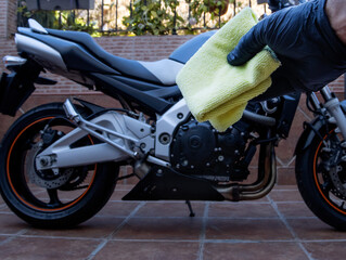 A hand with black latex gloves holds a yellow mop for cleaning and drying a motorcycle. A motorcycle in the background. Maintenance and cleaning concept.