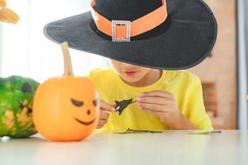Boy making jack o lantern at home white kitchen, cutting real pumpkins and playing with paper black...