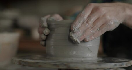 Close-up of potter's hands creating pot from clay concentrated on manufacturing ceramics using pottery wheel. Creative occupation and handmade goods concept.