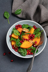 Seasonal winter persimmon salad with spinach, pomegranate seeds and walnuts in a bowl on a black background. New Year and Christmas menu