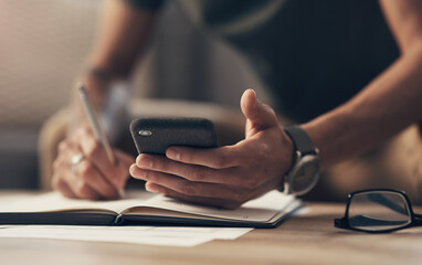 Phone, hands and student writing notes on book for learning, remote education or research. Mobile, pen and closeup of man with notebook for knowledge, study app and test preparation on table in home