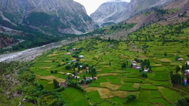 A sweeping aerial drone view over a lush patchwork agricultural valley bordered by dramatic, rugged rocky cliffs.