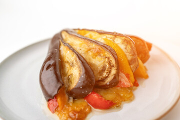 A plate of food with a variety of vegetables, including peppers and eggplant. The dish is served on a white plate and he is a healthy and colorful meal.