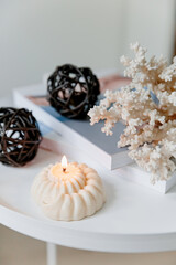 White cozy home concept. Burning candle light, coral, white table, books. Copy space