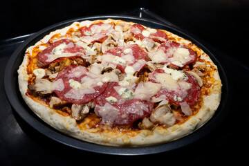 Pizza with cheese, salami, Tomato sauce, mushrooms, Flavors. Italian pizza on black surface.