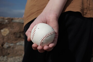 boy holding a baseball behind his back, back view, hands with a white ball.......
