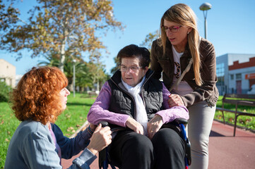 Two women assisting senior woman in wheelchair in park