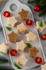 Christmas star shaped cheese and ham mini sandwiches on a ceramic board on a gray background. Festive food. Selective focus.