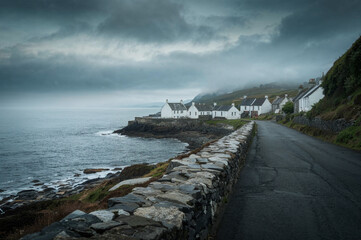 Small seaside Scottish style fishing village. Misty foggy early morning cloudy and cold sky and background. Houses near the ocean shoreline. With breakwater. Stone and concrete street.