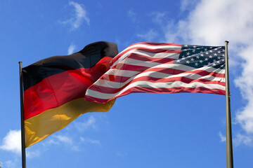 Gegeneinander wehende, käpfende Flaggen. US-Flagge und Deutschland-Flagge.