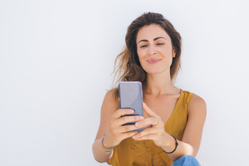 Pleased female in casual wear taking selfie on white wall