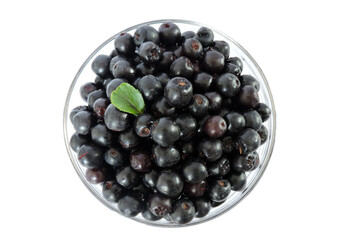 Fresh aronia berries decorated with a green leaf in a glass bowl, white background, top view