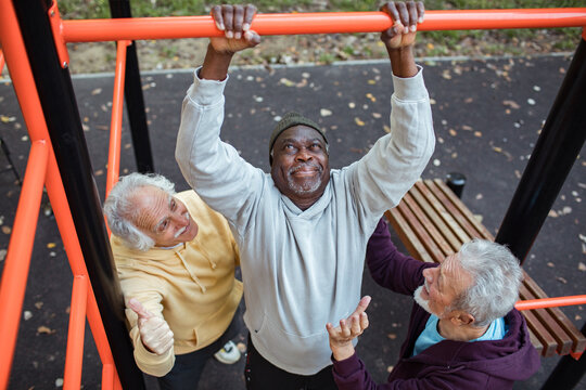 Senior men exercising together on pull-up bar in outdoor park fitness area