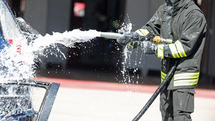 firefighter in uniform spraying fire extinguishing foam on a damaged car