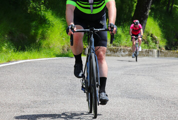 cyclist wearing sports clothing and black shorts cycling on a road bike uphill in summer