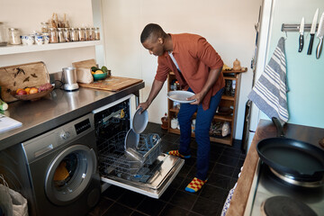Young African man putting some plates in a dishwasher at home