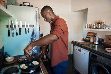 Young African man cooking eggs in a frypan on his stove