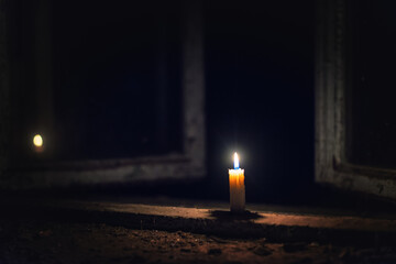 A candle burns in an abandoned place on an old and dirty window sill.